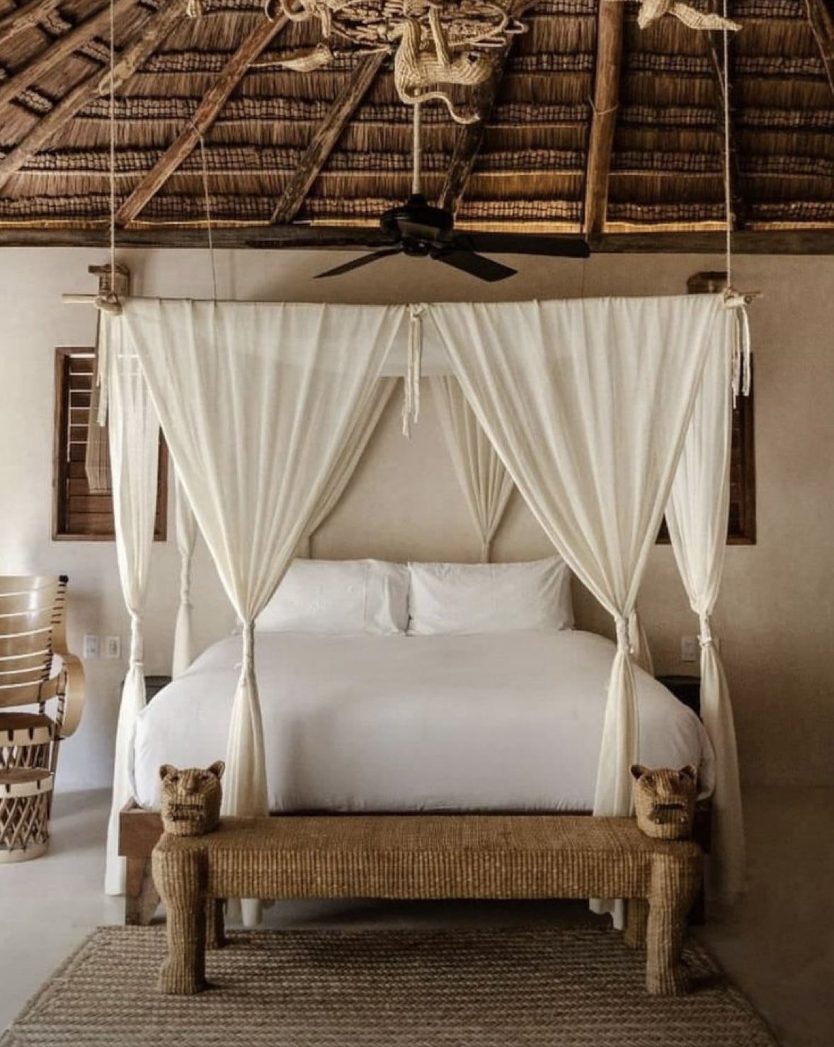 A bed with white curtains and two cats on the side.